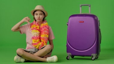 Çiçekli çiçek desenli genç kız mor bavulun yanına oturur ve baş parmak işareti gösterir. Krom anahtar yeşil ekran yeşil ekran stüdyo arka plan modelinde izole edilmiş. Yavaş çekim