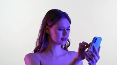 Bir kadın canlı ve renkli ışıklandırmayla işaretlenmiş bir telefonla meşgul oluyor. Görüntü modern teknolojiyi ve etkileşimi sembolize ediyor..