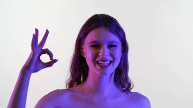 Bir kadın pırıl pırıl mor ve pembe ışıkta banyo yaparken gülümser, modern ve sanatsal bir etki yaratır..