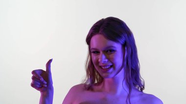 Bir kadın pırıl pırıl mor ve pembe ışıkta banyo yaparken gülümser, modern ve sanatsal bir etki yaratır..