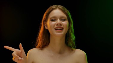 Uzun kahverengi saçlı, yaratıcı ve renkli ışıkların altında sıcak bir gülümsemesi olan genç bir kadın. Neşeli ifadesi mutluluğu ve pozitifliği yansıtıyor..