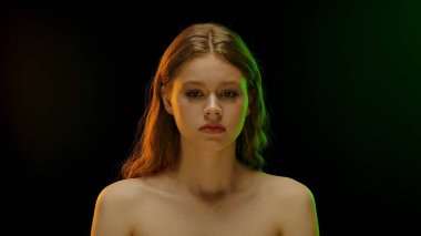 Bir kadın, çarpıcı mavi ve mor ışığın yoğun bir atmosfer yarattığı düz bir zemine dayanır..