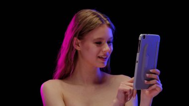 Bir kadın siyah arkaplanla işaretlenmiş bir tabletle meşgul. Görüntü modern teknolojiyi ve etkileşimi sembolize ediyor..