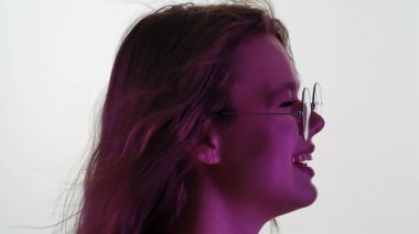 Gözlüklü, uzun saçlı, rüzgarda süzülen, yumuşak mor ışık altında bir kadının profil fotoğrafı. Yan görünüm