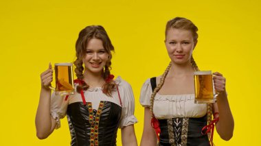 Geleneksel kıyafetler giyen iki kadın bira bardakları tutuyor, parlak sarı bir arka plan önünde gülümsüyorlar..