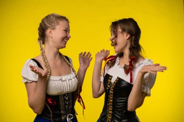 Parlak sarı bir arka planda geleneksel kostümler giyen iki kadın neşeyle etkileşime girer..