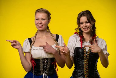 Geleneksel Bavyera ağıtlarında canlı sarı bir arka plana gülümseyen neşeli enerji saçan iki kadın..