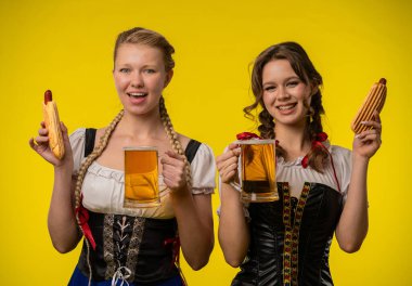 Geleneksel giyinmiş iki kadın, bayram ruhunu kucaklayan içeceklerin ve sosislilerin tadını çıkarıyorlar..