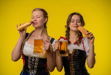 Geleneksel giyinmiş iki kadın, bayram ruhunu kucaklayan içeceklerin ve sosislilerin tadını çıkarıyorlar..