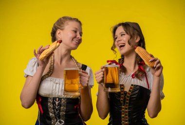 Geleneksel giyinmiş iki kadın, bayram ruhunu kucaklayan içeceklerin ve sosislilerin tadını çıkarıyorlar..
