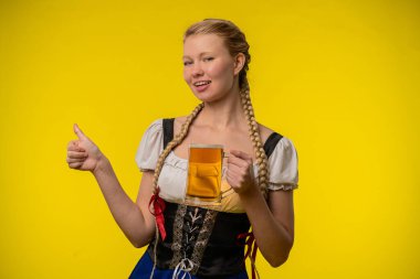Bavyera kıyafetli neşeli bir kadın elinde parlak sarı bir arka planda bira bardağı tutuyor. Gülümsüyor ve başparmak işareti yapıyor, neşeli ve hayat dolu bir atmosferi simgeliyor..