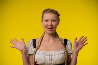 Saçları örgülü ve şaşırmış bir kadın elleri parlak sarı bir arka planda duruyor..