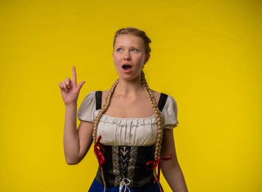 Geleneksel saç örgülü bir kadın, elleri parlak sarı bir arka planda hareket eden, şaşırmış bir yüz ifadesi sergiler..