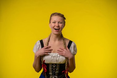 Neşeli bir kadın, parlak sarı bir arka plana karşı duruyor, örgülü geleneksel bir elbise giyiyor..