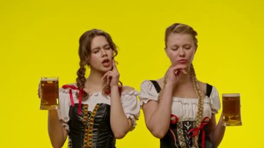 Geleneksel kıyafetler giyen iki kadın bira bardakları tutuyor, parlak sarı bir arka plan önünde gülümsüyorlar. Yavaş çekim