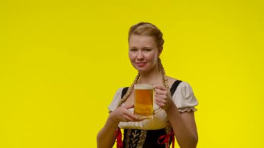 Geleneksel bir kıyafet giymiş bir kadın elinde bira fincanı tutarken gülümsüyor, parlak sarı bir arka planda duruyor. Yavaş çekim