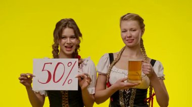 Geleneksel elbiseli iki kadın sarı arka plana karşı 50 tabela tutarak özel bir teklif sunuyor..