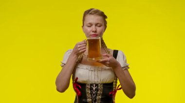 Bavyera Dirndl elbisesi giymiş genç bir kadın, parlak sarı bir arka planda büyük bir bardak biranın keyfini çıkarıyor..