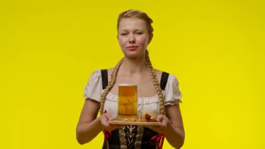 Geleneksel Bavyera kıyafeti giymiş bir kadın elinde bir bardak bira ve sarı arka planda bir kraker tutuyor..
