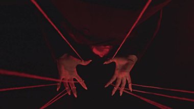 Kırmızı iplerden oluşan bir ağ boyunca hareket eden, karmaşık bağlantıları ve hareketleri sembolize eden büyüleyici bir el görüntüsü..