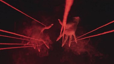 Gizemli ve atmosferik bir sahne. Parlayan kırmızı tellerle çevrili, kıvrımlı dumanla çevrili eller..