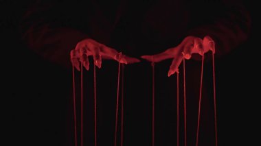 Ellerin kırmızı dizgileri kontrol ettiğini gösteren gizemli bir resim, karanlık ışık altında manipülasyon temaları çağrıştırıyor.