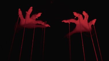 Kırmızı ışıkta ellerin sanatsal tasviri ipleri manipüle ediyor, kontrol ve gizem hissi uyandırıyor..