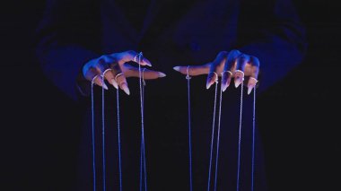 Bu resim, mavi ışık altında kukla dizilerini manipüle eden, kontrol ve manipülasyon temaları anımsatan uzun tırnaklı elleri gösteriyor..