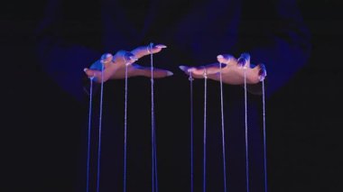 Eller, kontrol ve yönlendirme kavramını temsil eden karanlık bir uzayda ipleri manipüle eder. Yavaş çekim