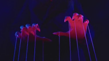 Uzun tırnakları olan, dramatik ve karanlık ışıklarda ipleri manipüle eden büyüleyici bir el görüntüsü. Atmosfer ürkütücü ve merak uyandırıcı, kontrol ve gizemi çağrıştırıyor. Yavaş çekim