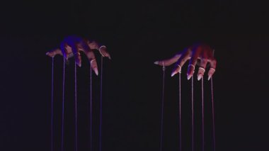 İpleri manipüle eden, karanlık ve esrarengiz bir ortamda kukla ustasına benzeyen ellerin görüntüsü. Yavaş çekim