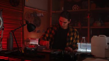 Genç bir adam retro fotoğraf stüdyosunda oturuyor ve sıcak ışık altında telefonuna bakıyor..