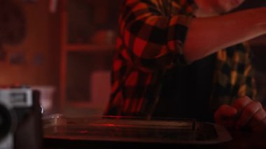 Genç bir adam retro fotoğraf stüdyosunda oturuyor ve sıcak ışık altında telefonuna bakıyor..