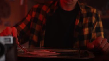 Ekose gömlekli bir insan, sıcak, karamsar ışıklandırma altında lens ayarlarına odaklanan klasik bir kamera montajı üzerinde çalışır..