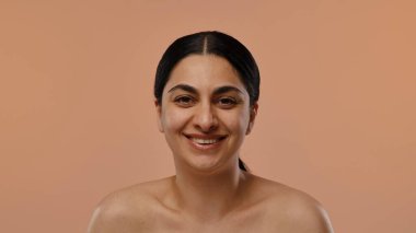 Sıcak turuncu arka planda siyah saçlı gülümseyen bir kadının neşeli portresi..