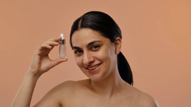 Bir kadın elinde küçük bir şişe cilt serumu tutarken gülümsüyor..