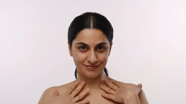 Kendine güvenen bir ifade ve doğal güzelliğe sahip bir kadın tarafsız bir arkaplana karşı rahat bir şekilde poz verir..