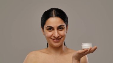 Bir kadın elinde bir krema kavanozu tutarken gülümser. Işıl ışıl ifadesiyle güzelliği ve refahı teşvik eder..