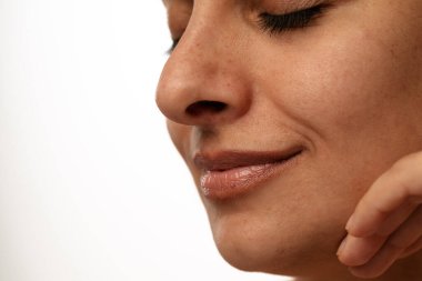 Doğal bir şekilde gülümseyen, cilt dokusunu ve yüz hatlarını vurgulayan bir kadının yakın plan görüntüsü..