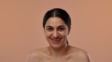 Sıcak turuncu arka planda siyah saçlı, gülümseyen bir kadının neşeli portresi. Yavaş çekim