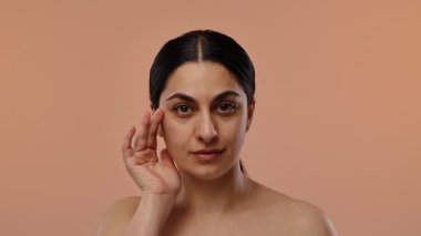 Görüntüde koyu saçlı bir kadın var. Yumuşak şeftali arka planına hafifçe dokunuyor. Yavaş çekim