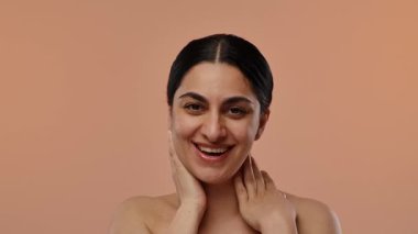 Neşeli bir kadın gözleri kapalı gülümser, boynuna nazikçe dokunur sıcak bir arka plana. Yavaş çekim