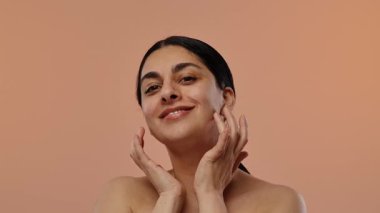 Neşeli bir kadın gözleri kapalı gülümser, boynuna nazikçe dokunur sıcak bir arka plana. Yavaş çekim