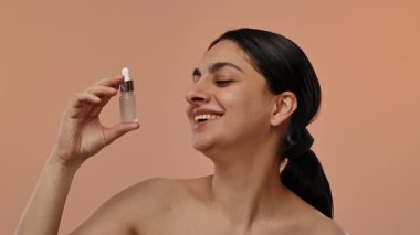 Bir kadın, elinde küçük bir şişe cilt serumuyla çekici bir arka plana gülümsüyor. Yavaş çekim