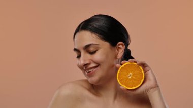 Kapalı gözlü bir kadın elinde taze bir portakal dilimiyle gülümseyerek huzurlu ve sağlıklı bir anın tadını çıkarıyor. Yavaş çekim