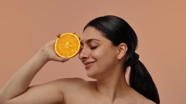 Neşeli bir suratı olan bir kadın şeftali arka planında bir dilim portakal tutuyor. Yavaş çekim