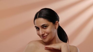 Neşeli bir yüzü olan bir kadın, sıcak ve yumuşak bir arka planda el hareketi yaparken gülümsüyor. Yavaş çekim