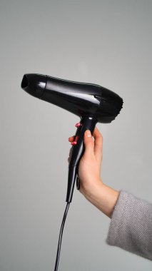 Siyah bir saç kurutma makinesi tarafsız bir arkaplan karşısında el ele tutuşur, parlak tasarımı ve işlevselliği vurgular..