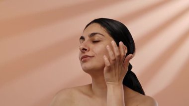 Doğal poziyondaki bir kadının, ifadesini geliştiren bej bir arka plan tarafından vurgulanmış sakin bir portresi. Yavaş çekim