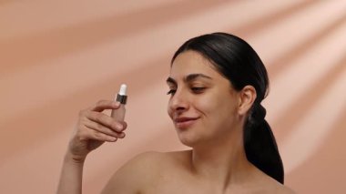 Bir kadın elinde küçük bir kozmetik serumu şişesi tutuyor, deri sağlığını iyileştirmek için günlük cilt bakımında kullanıldığını gösteriyor. Yavaş çekim